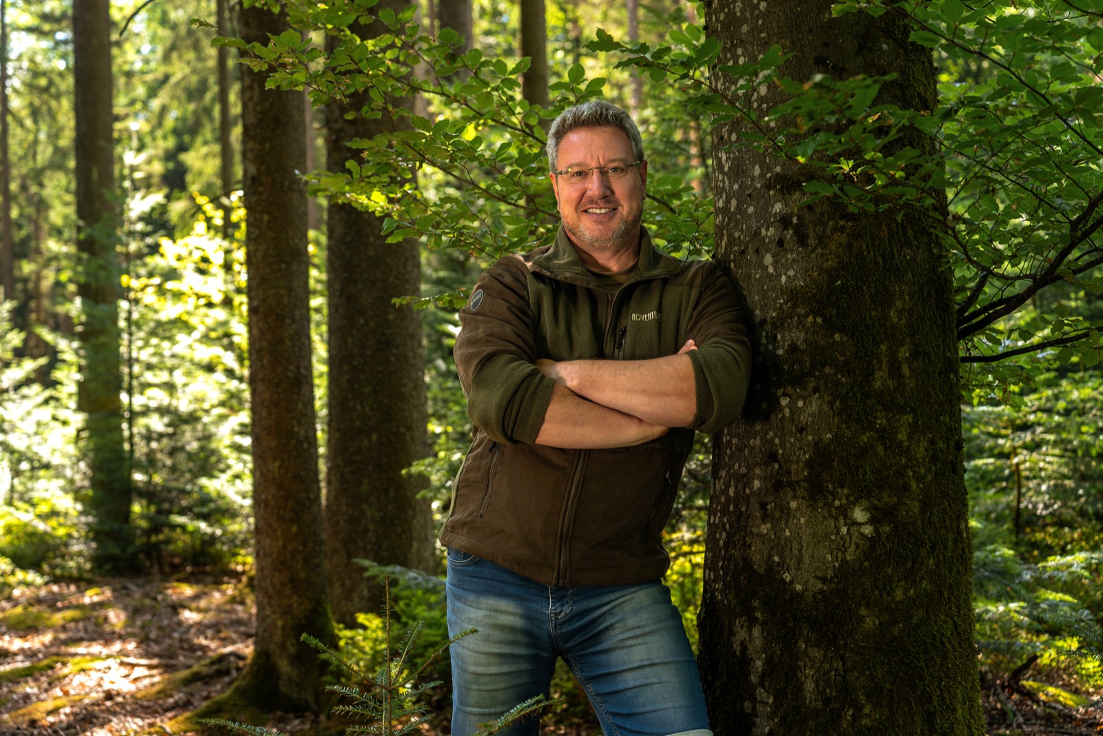 Winfried Steimler steht an einen Baumstamm gelehnt in seinem Wald